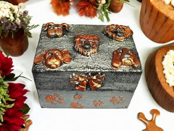 A small , rectangular wooden box painted in silver colour, decorated with air dry clay puppy faces on the lid and paw prints along the sides.