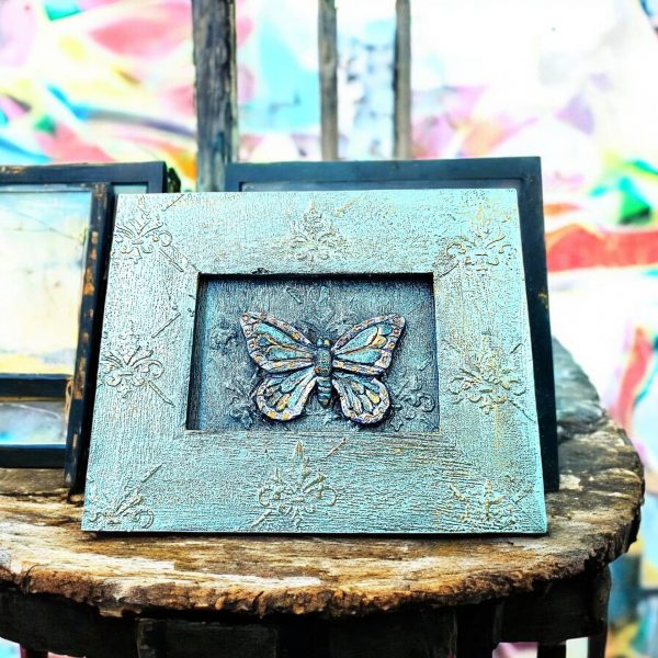 A handcrafted picture frame with a textured, rustic appearance, gold accents, and central butterfly design