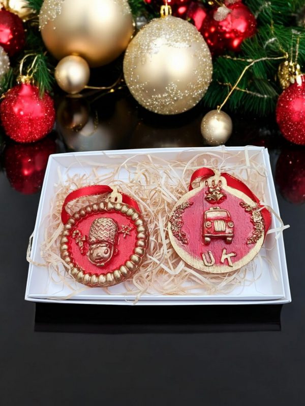 Set of two British- themed Christmas baubles featuring a royal guard and London taxi in red and gold.