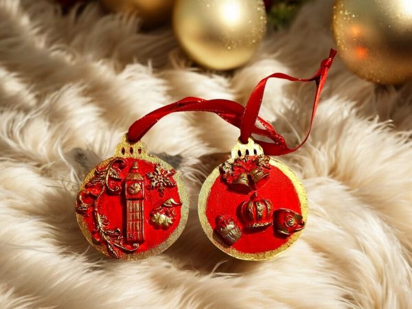 Two handcrafted Christmas tree ornaments with a red background and gold accents, featuring designs of Big Ben and British crown with holiday motifs.