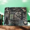 a small , three-dimensional artwork featuring miniature metal tools and objects, including a saw, drill, hammer, wrench, barrel, ladder and gears, arranged on a rectangular base.