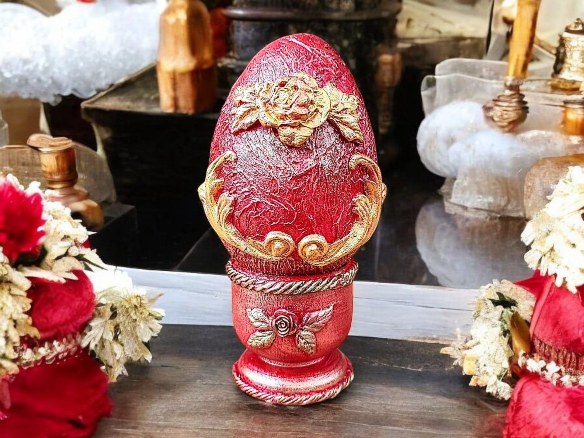 Handcrafted red decorative egg with gold floral details on a matching stand, set against a floral backdrop.